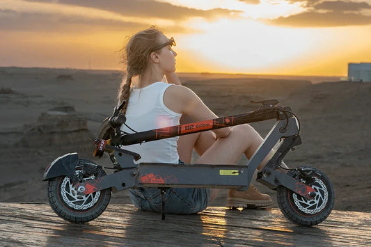 Woman sits beside Kukirin G2 Ultra electric scooter enjoying desert sunset view