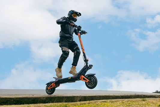 Full protective gear rider performs an airborne jump stunt on black-and-orange Kukirin G3 Pro electric scooter against bright blue sky with clouds.