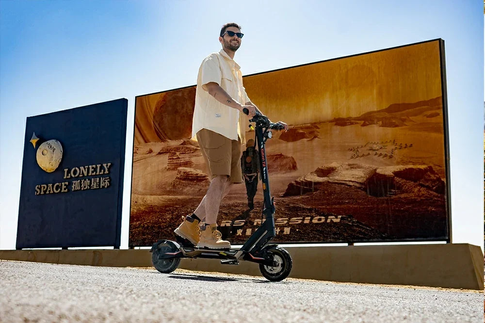 Man riding Kukirin T3 electric scooter in front of Mars-themed space billboards