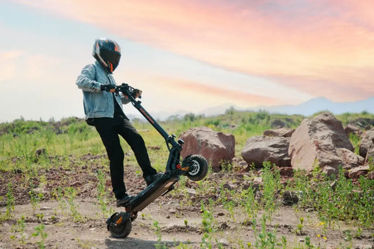 Kukirin G2 Master off-road electric scooter wheelie on a rocky mountain trail at sunset.