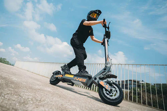 Kukirin G2 grey sport electric scooter with orange graphics, rider wearing full helmet climbing concrete ramp under blue sky.