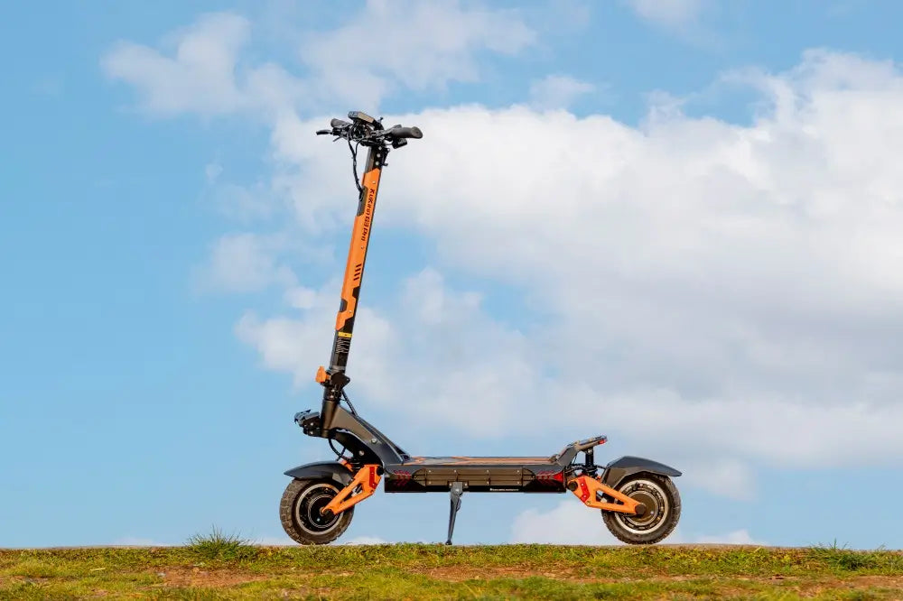Kukirin G3 PRO dual-motor off-road electric scooter with orange frame, standing on grass against a cloudy blue sky.