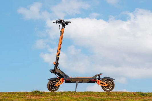 Kukirin G3 PRO dual-motor off-road electric scooter with orange frame, standing on grass against a cloudy blue sky.