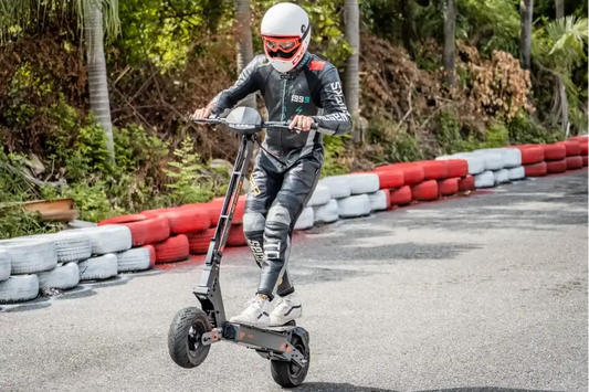 Dynamic racing action shot of rider wheeling matte grey Kukirin G4 performance electric scooter on asphalt kart track lined with red-white tire barriers.
